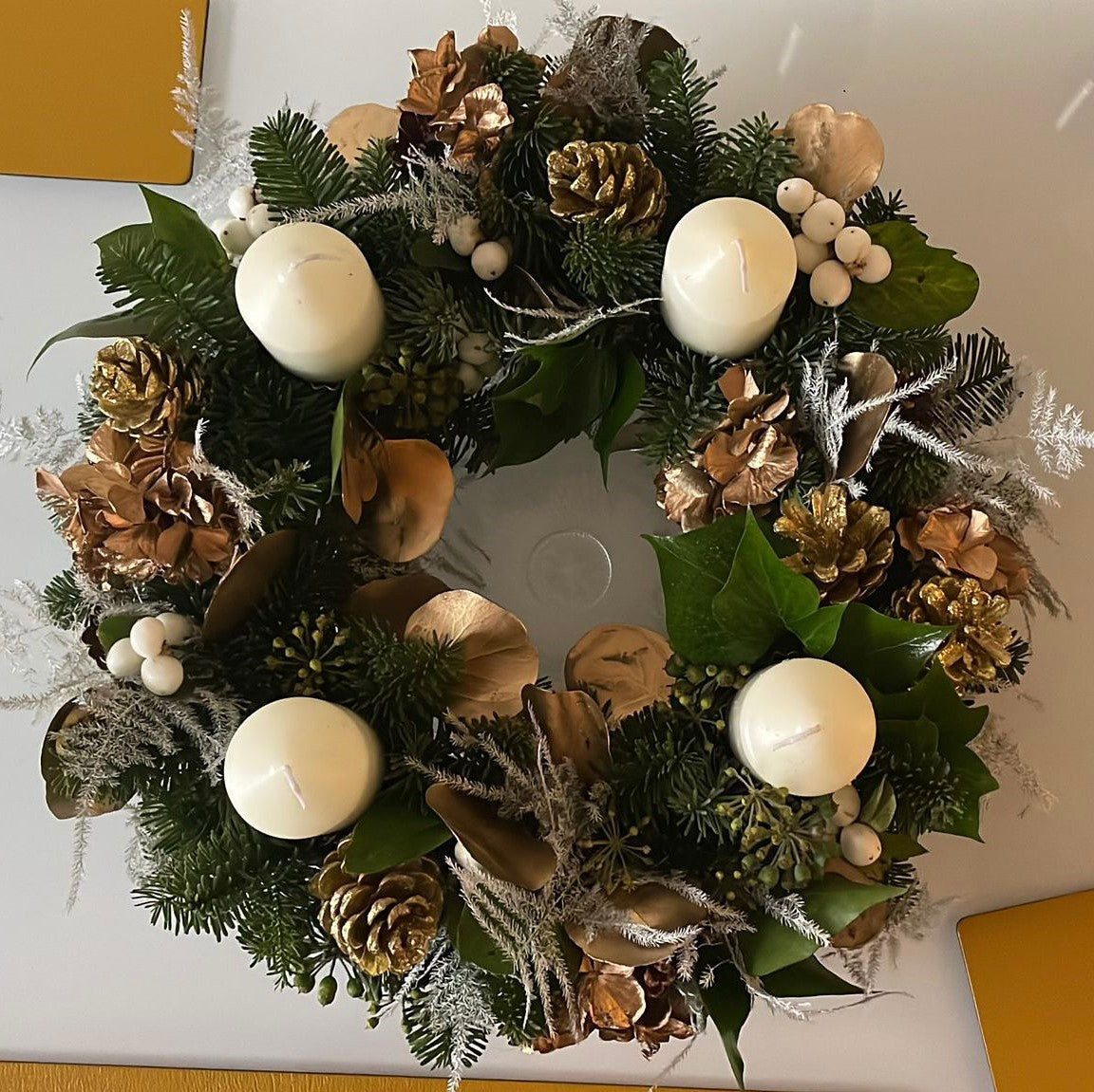 'Andrew's Natural Advent Wreath' is a pine Advent Wreath with 4 ivory pillar candles, gold pine cones, copper eucalyptus, white hypericum berries and silver asparagus fern.