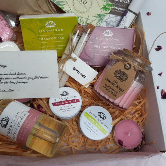 A close-up of our letterbox gift, including treats like organic scented soy candle, lip balm, handmade soap and shampoo bars, chocolates, bath salts, shower steamers, and infuser oils.