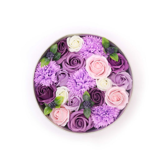 This round, hat box is full of lavender roses and carnations in different shades of purple. An elegant gift for an anniversary.