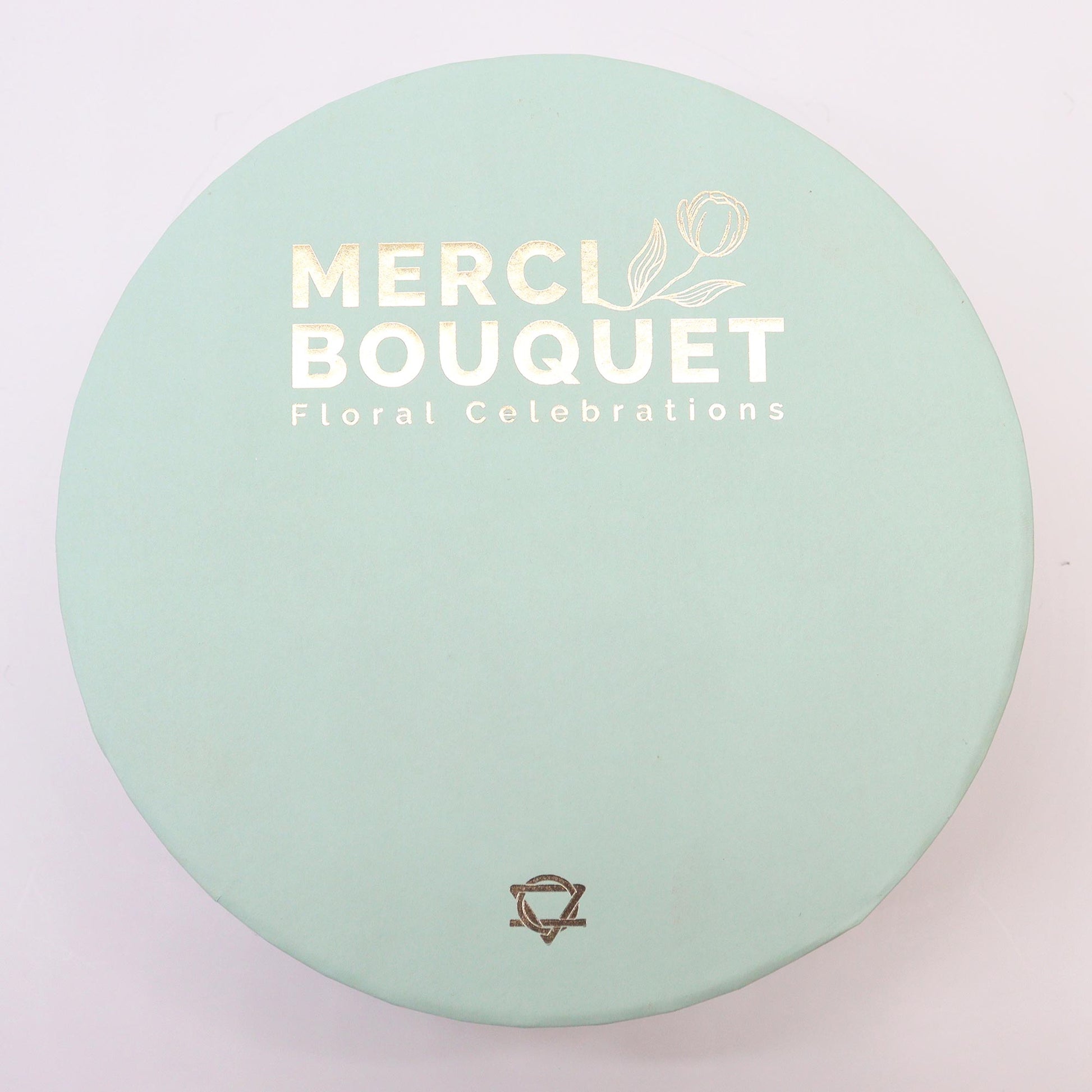 A green hatbox lid, with a white title saying Merci Bouquet Floral Celebrations. Inside the hat box are soap Roses and carnations in yellows, pinks, whites, and greens. A lovely gift for any celebration.